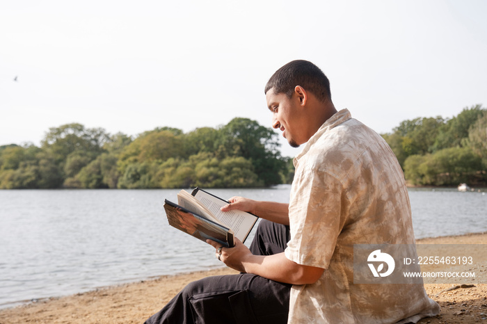 Man reading book on lakeshore