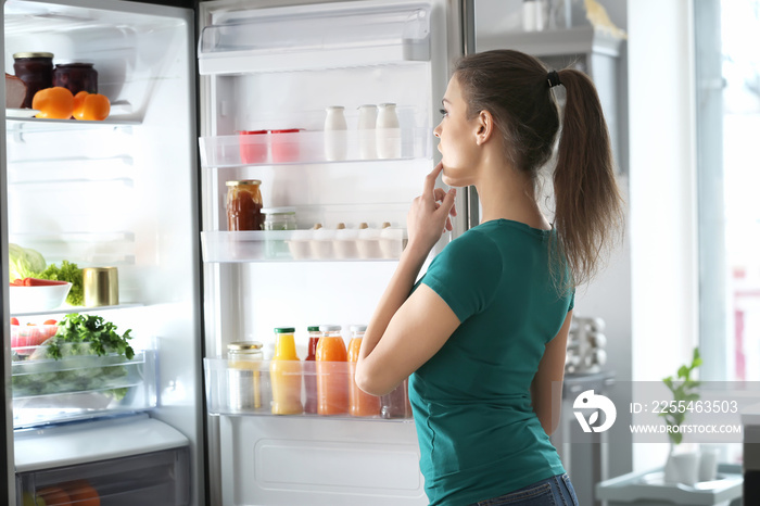 Woman standing near open fridge at home