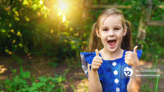 Laughing little caucasian girl walking in the garden, degree thumbs up.