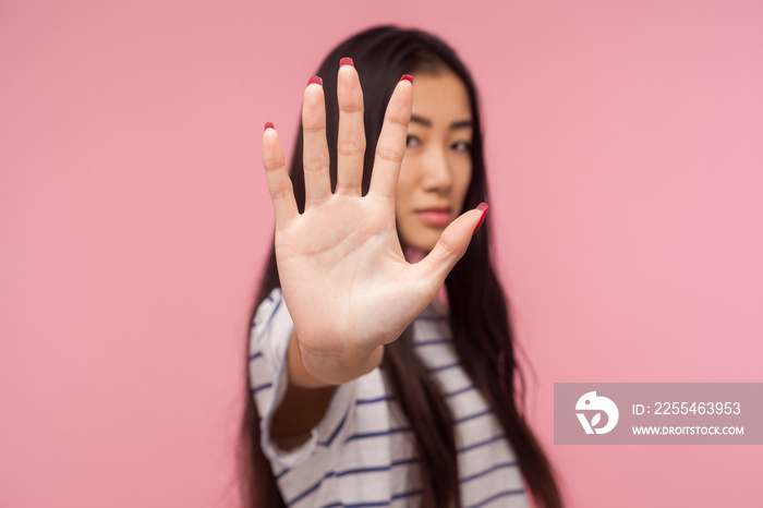 Ban, prohibition concept. Portrait of serious girl with brunette hair holding out hand, showing Stop, block gesture, warning of danger, refusing to communicate. studio shot isolated on pink background