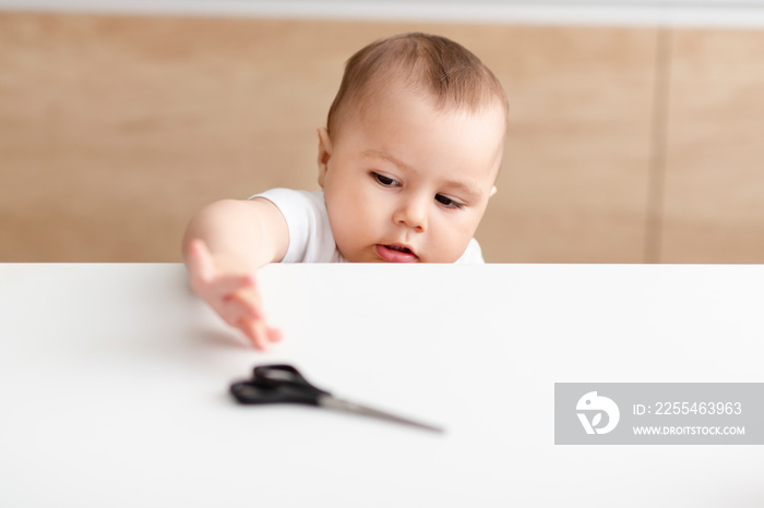 Baby boy trying to get scissors from kitchen table