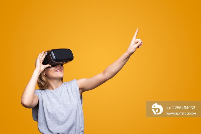 Smiling woman wear virtual reality headset explore new horizons isolated over yellow background. Technology concept.