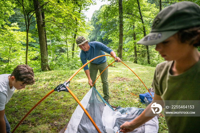 Air Force service member sets up a tent with his sons on  a backpacking trip.