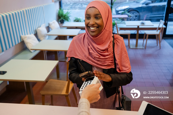 Smiling female customer paying with smart phone in cafe