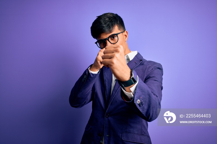 Young handsome business man wearing jacket and glasses over isolated purple background Punching fist to fight, aggressive and angry attack, threat and violence