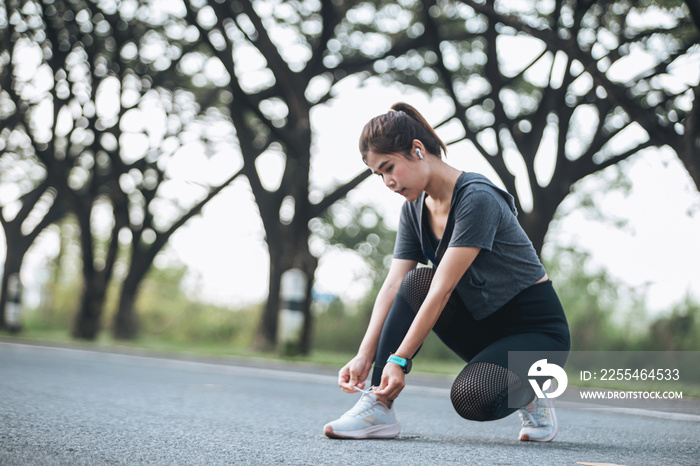 Mature fitness woman tie shoelaces on road. Cheerful runner sitting on floor on city streets with mobile and earphones wearing sport shoes. Active latin woman tying shoe lace before running.