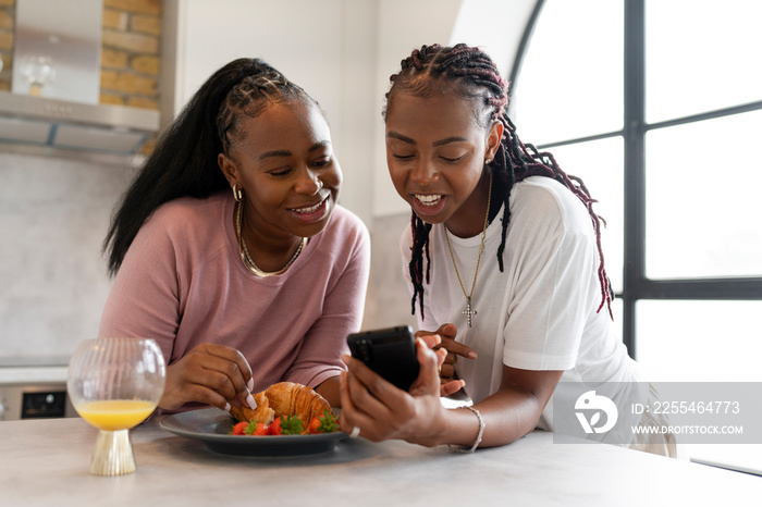 Lesbian couple using phone during breakfast in kitchen