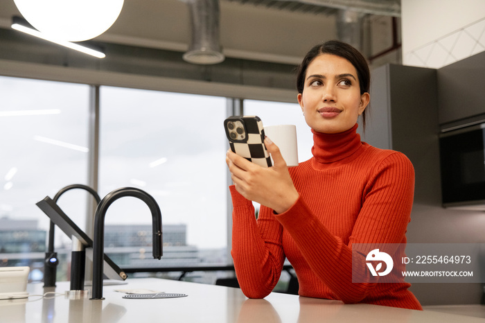 Woman using smart phone in office kitchen