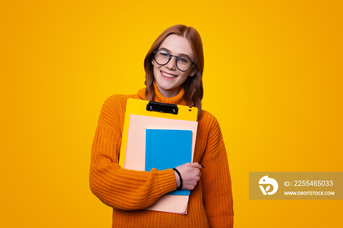 Happy woman wearing eyeglasses standing holding notepads smiling at camera isolated over orange color background studio portrait. Creative concept idea