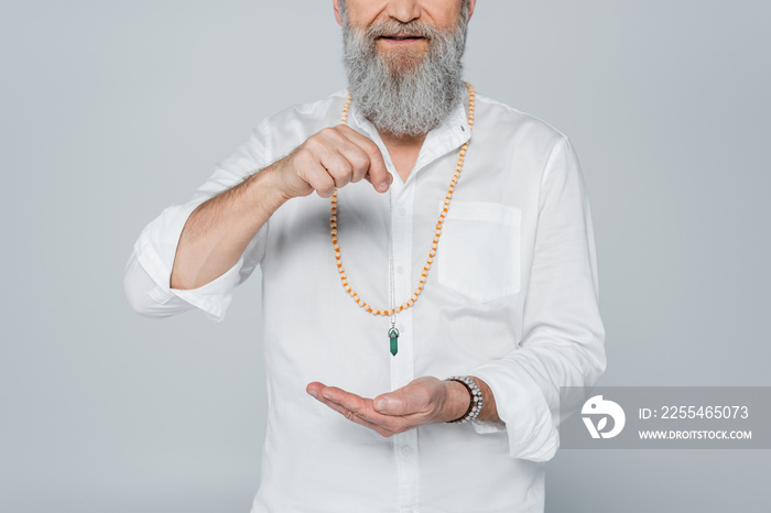 partial view of bearded spiritual guru holding dowsing pendulum isolated on grey.