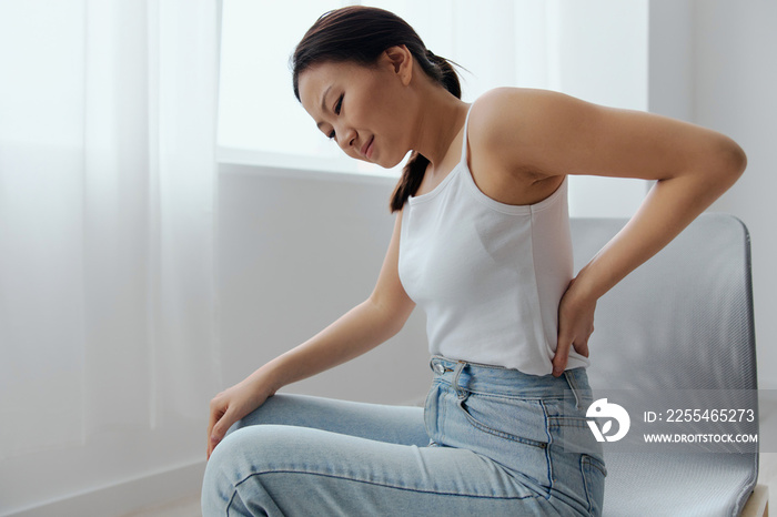 Suffering from scoliosis osteochondrosis after long study pretty young Asian woman feel hurt joint back pain laptop in incorrect posture sit on chair. Injuries Poor health Illness concept. Cool offer