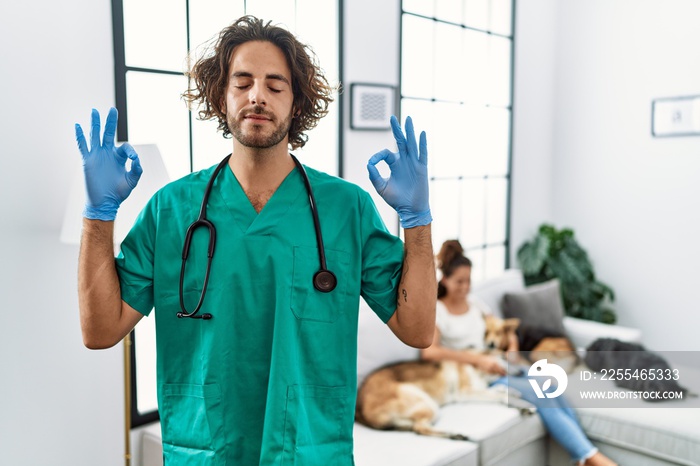 Young veterinarian man checking dogs at home relax and smiling with eyes closed doing meditation gesture with fingers. yoga concept.