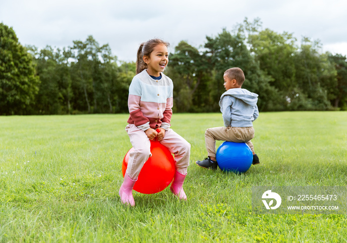 childhood, leisure and people concept - happy children bouncing on hoppers or bouncy balls at park