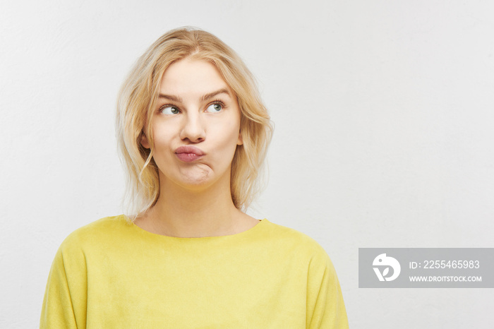 Portrait of an embarrassed young woman with a confused mouth in yellow clothes on a white background with free space for your text