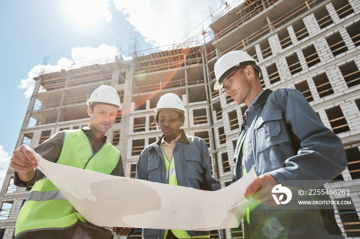 Low angle view at diverse group of engineers discussing floor plans at construction site