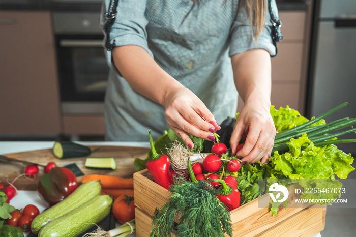 Woman unpacking fresh vegetables from wooden crate.  Unrecognizable woman taking organic vegetables out of the wooden box in the kitchen. Zero waste and sustainable lifestyle concept, home delivery