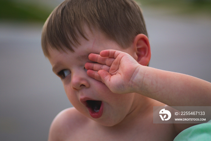 Young child toddler yawns and rubs his eye outside