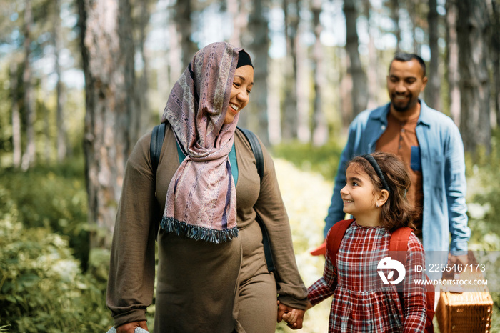 Happy Middle Eastern mother and daughter communicating while holding hands during family walk in nature.