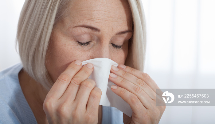 Healthcare, cold, allergy and people concept, sick woman blowing her runny nose in paper tissue on white background