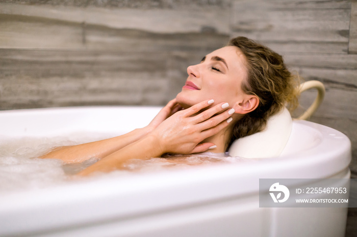 Close up of beautiful young lady relaxing at thermal bath in a beauty center, touching face, smiling