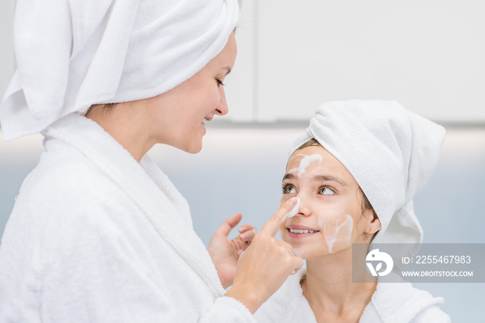 Happy mother applies on face her daughter wash foam in the bathroom at home