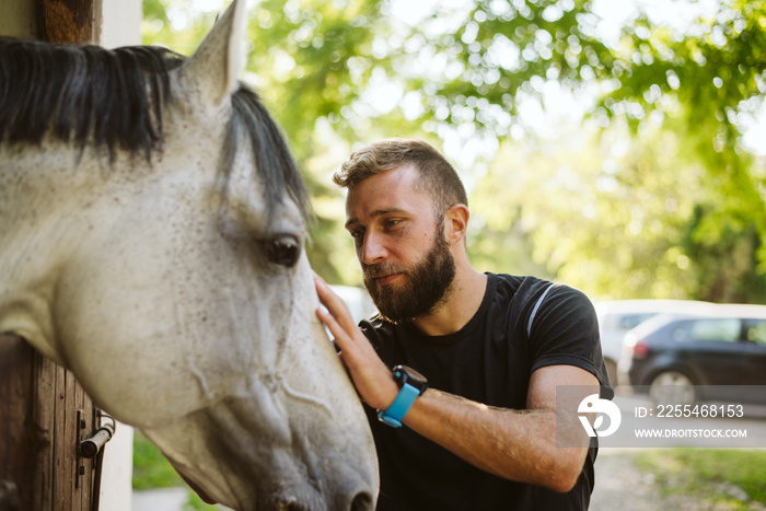 A bearded man petting his handsome white horse on a farm