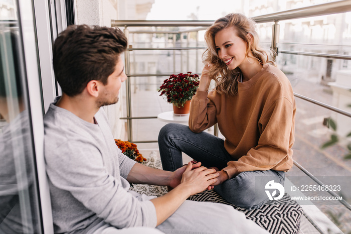 European man touching girlfriend’s hands. Smiling debonair woman talking with friend at balcony.