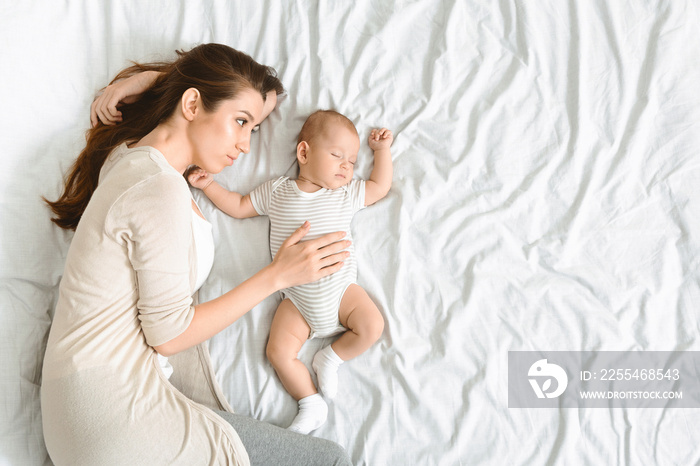 Young mother tenderly hugging her sleeping newborn baby