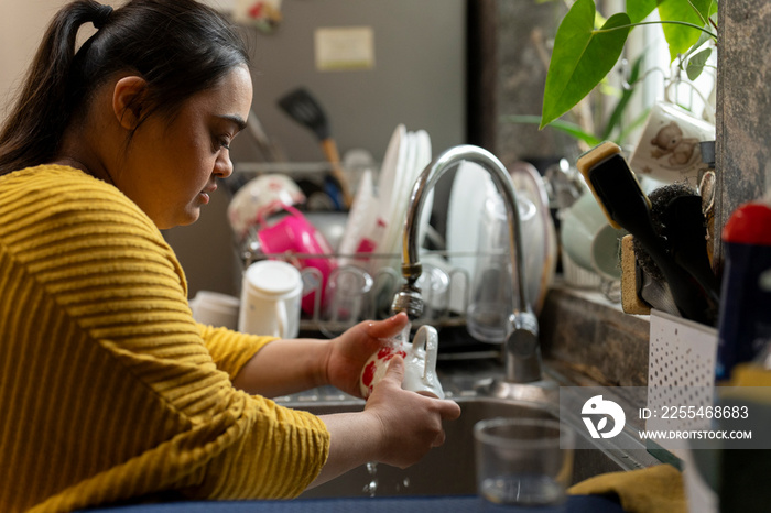 Young woman with down syndrome washing dishes at home