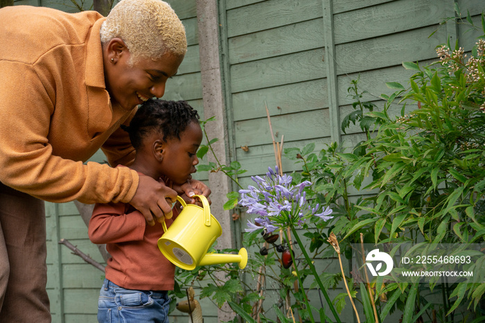 Mother and daughter (2-3) watering plants in garden