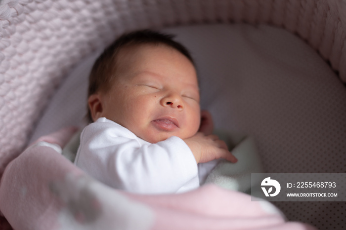 closeup portrait of beautiful and adorable newborn baby girl with mixed Asian Caucasian ethnicity lying on bassinet covered with blanket days after coming to life