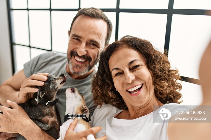 Middle age hispanic couple smiling happy making selfie by the camera. Lying on the bed with dogs at home.