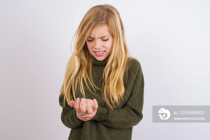 Caucasian kid girl wearing green knitted sweater against white wall Suffering pain on hands and fingers, arthritis inflammation