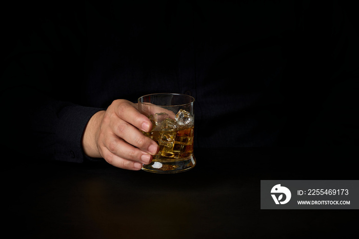 close-up of a man’s hands with a glass of Scotch and ice on a dark background