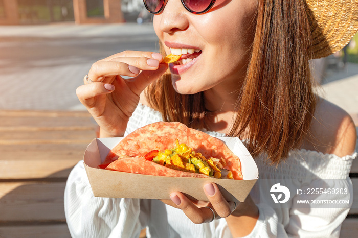 Happy asian girl eating taco outside. Mexican fastfood cuisine. Tasty and spicy snack in park