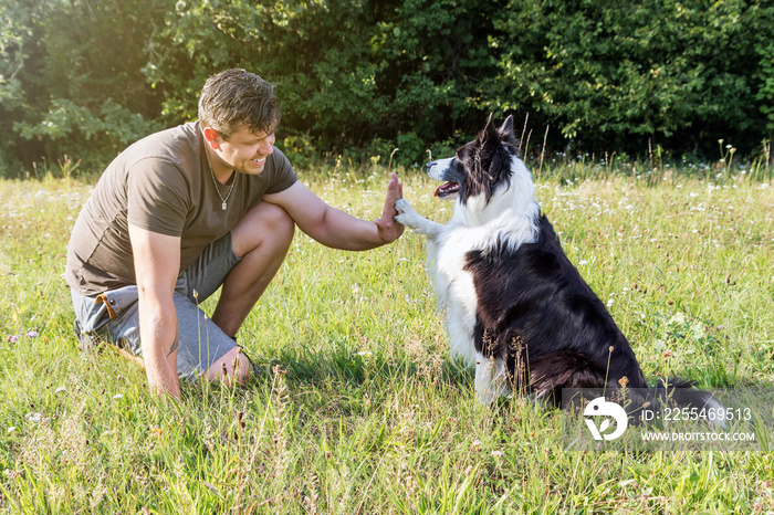 High five with the cute Border Collie and young man outdoors.