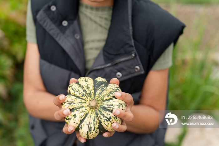 Mid section of woman holding homegrown gourd in urban garden