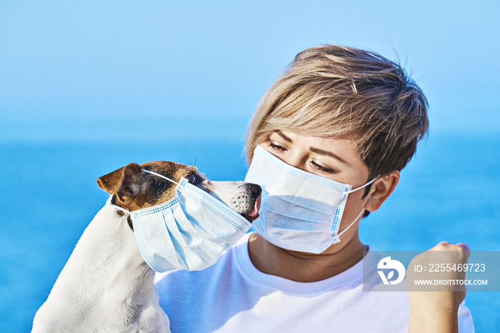 Woman in protective face mask looking at dog wearing medical mask