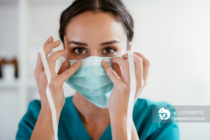 Young female doctor in medical office. Beautiful female doctor putting mask on. Close up.