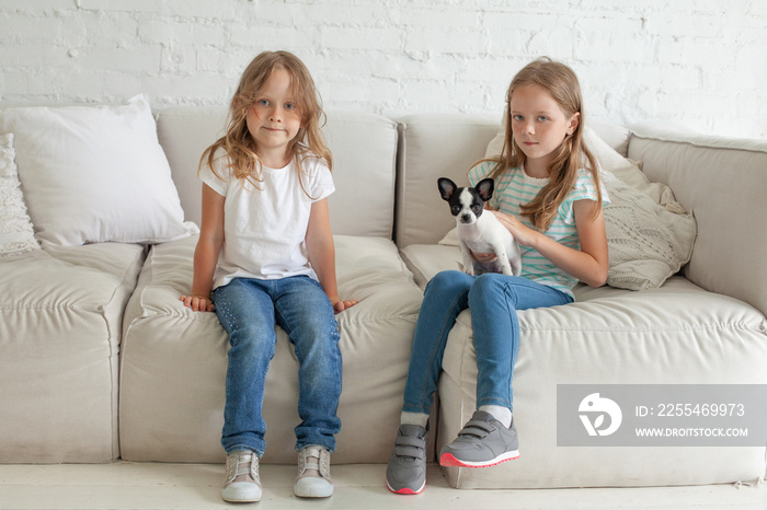 Cute little child girls with dog sitting on the sofa at home