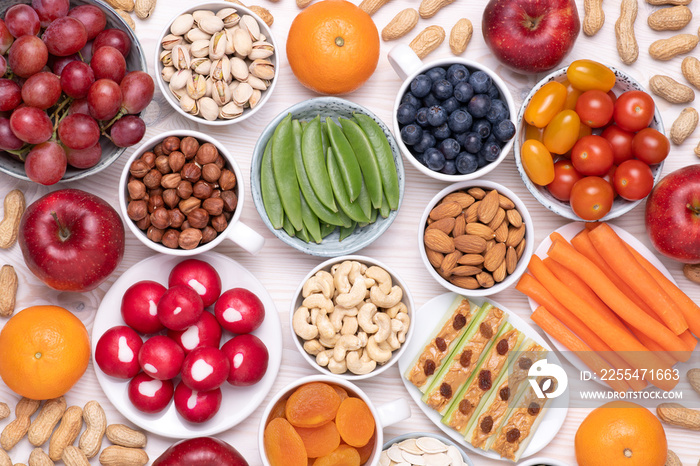 Healthy snacks such as fresh fruits, vegetables and nuts on white wooden table, top view