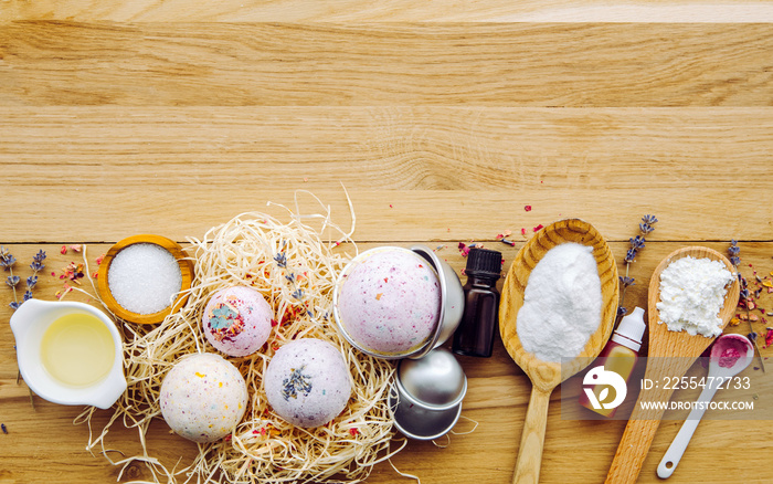 Making fizzy bath bombs at home concept. All the ingredients on table on wood spoons: cornstarch, essential oil, dye, citric acid, baking soda, dry herbs, round metal pressing molds. Copy space.