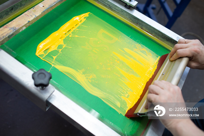 Serigraphy silk screen print process at clothes factory. Frame, squeegee and plastisol color paint