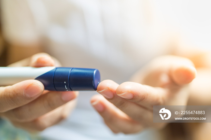 Close up of woman hands using lancet on finger to check blood sugar level by Glucose meter in the morning. Use as Medicine, diabetes, glycemia, health care and people concept.