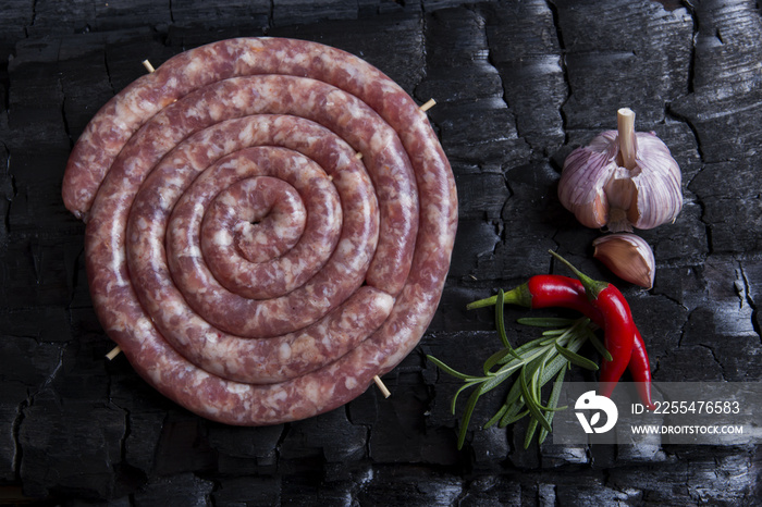 Freshly made raw spiral sausages in skins on a black background of charcoal