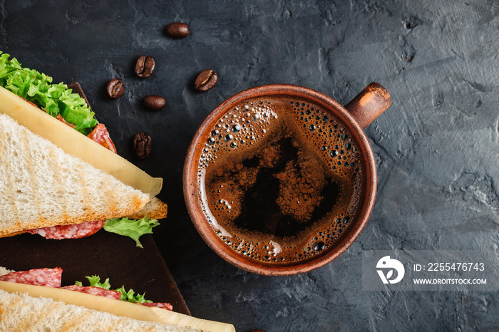 Cup with hot coffee and sandwich with grilled toast, salami sausage, salad lettuce and cheese on dark background, top view