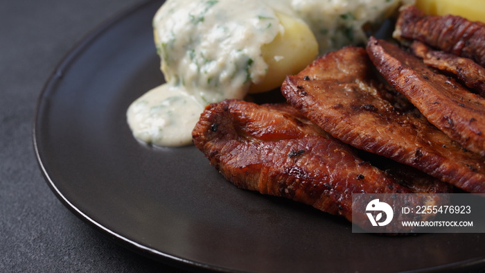 Crispy fried pork with creamy parsley sauce and boiled potato in the plate on the table or stegt flæsk, a classic Danish cuisine.