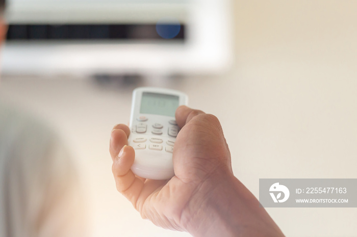 Close up of hand turn on air conditioner with remote control, maintenance concept.