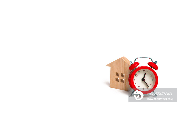 Wooden house and red alarm clock on a white background. The concept of rent housing monthly and hourly. Temporary affordable accommodation, hotels and hostels. A loan to buy a house.