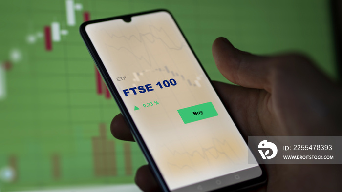 An investor’s analyzing the FTSE 100 etf fund on screen. A phone shows the FTSE 100 ETF’s prices to invest